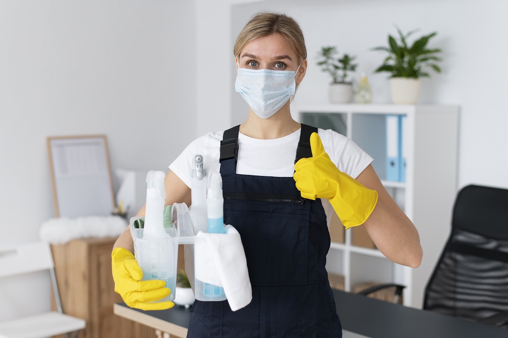 Imagem de uma mulher com produtos de limpeza, representando a diferença entre limpeza, desinfecção e higienização