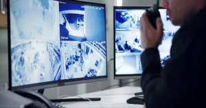 Vigilante fala pelo rádio enquanto faz o monitoramento de empresa por meio de circuito de câmeras de segurança