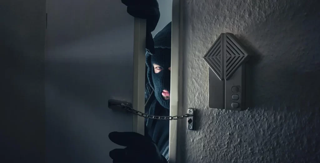 Criminoso encapuzado invade a porta de uma casa, ilustrando a importância do sistema antifurto