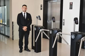 Porteiro recebendo pessoas ao lado de catracas para controle de acesso de visitantes em prédio