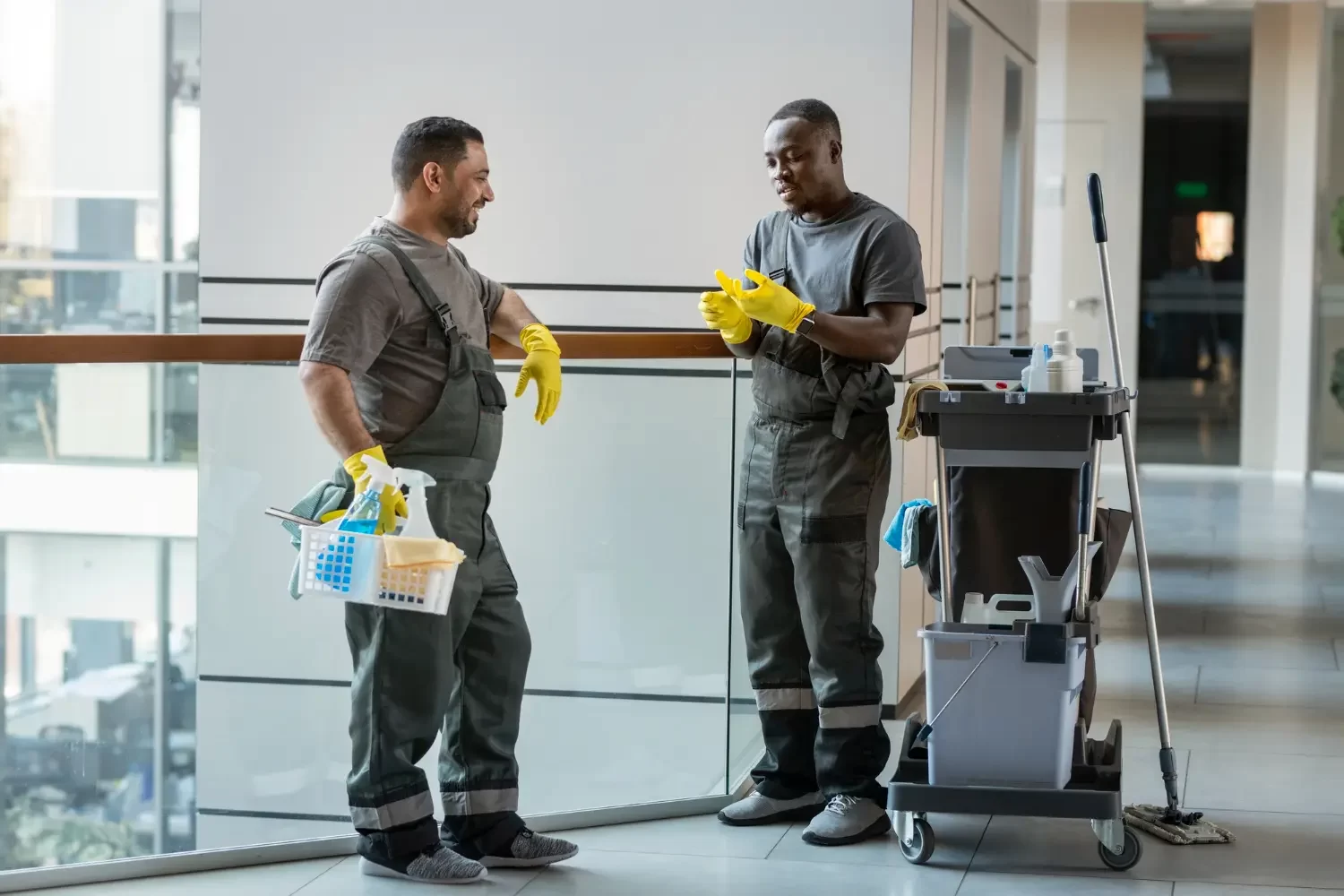 Dois profissionais de serviço de limpeza terceirizados sorrindo ao lado de equipamentos de limpeza.